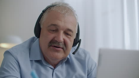 middle-aged-chubby-man-with-moustache-is-using-headphones-with-microphone-for-communicating-with-colleagues-at-online-chat